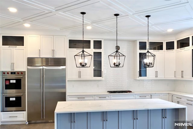 kitchen with appliances with stainless steel finishes, a center island, light stone counters, white cabinets, and decorative light fixtures