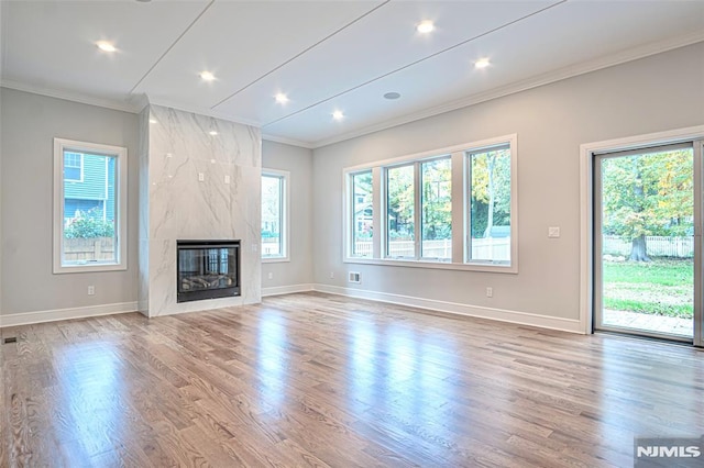 unfurnished living room featuring a high end fireplace, light wood-type flooring, crown molding, and plenty of natural light