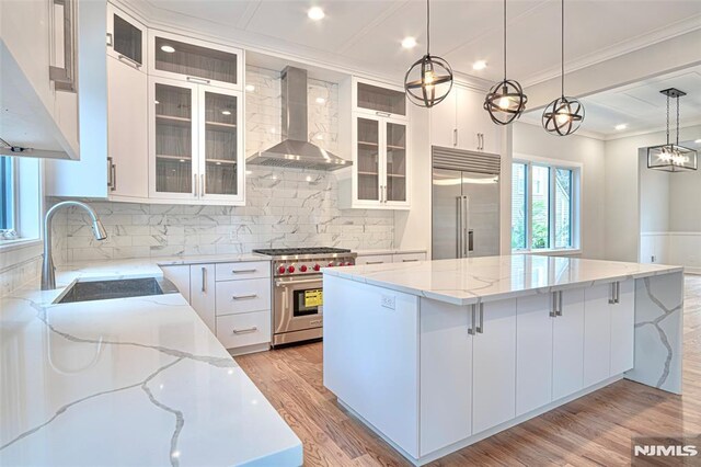 kitchen featuring high end appliances, wall chimney exhaust hood, decorative light fixtures, a spacious island, and white cabinets