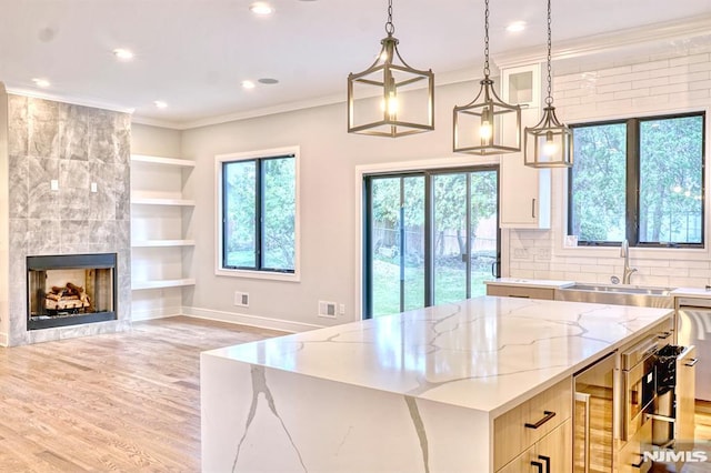 kitchen featuring a kitchen island, light stone counters, a tiled fireplace, and pendant lighting