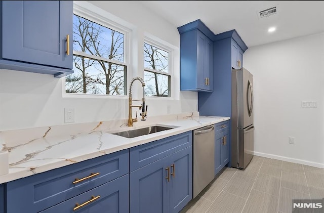 kitchen with light stone countertops, sink, blue cabinets, and appliances with stainless steel finishes