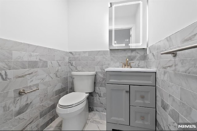 bathroom with vanity, tile walls, and toilet