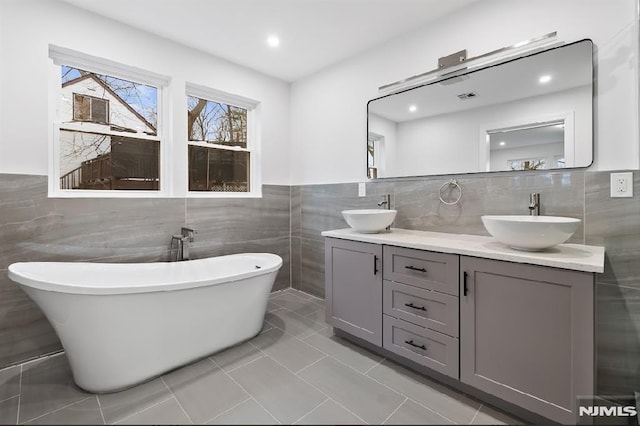 bathroom with tile patterned floors, a bathtub, tile walls, and vanity