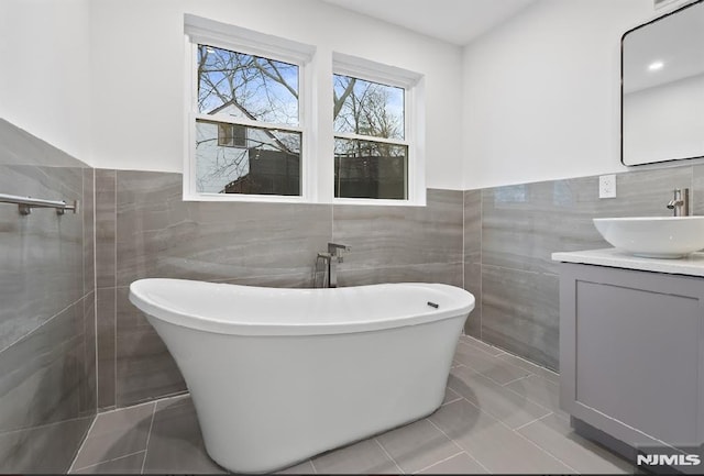 bathroom featuring a washtub, vanity, tile walls, and tile patterned flooring