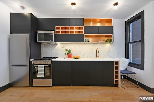 kitchen with backsplash, sink, light wood-type flooring, and appliances with stainless steel finishes