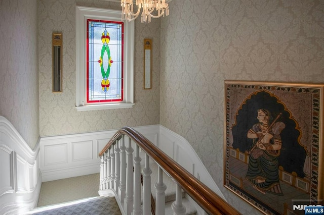 stairs featuring wainscoting, a chandelier, and wallpapered walls