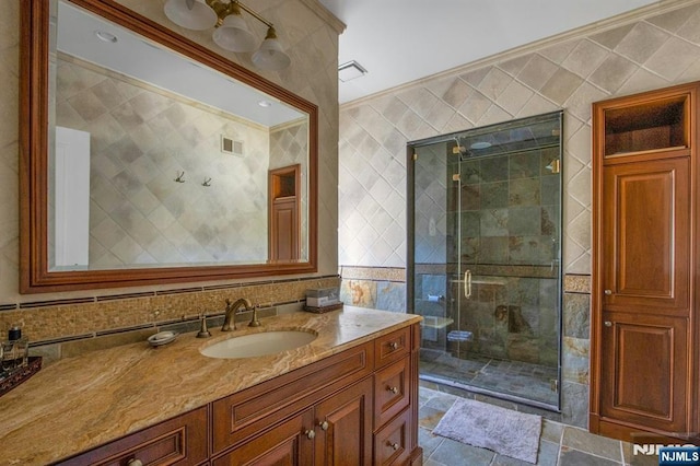 full bath featuring a stall shower, tile walls, visible vents, vanity, and crown molding