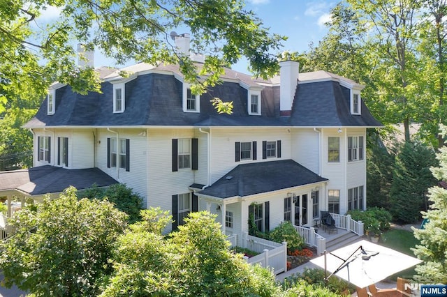 rear view of house featuring mansard roof, a chimney, and a shingled roof