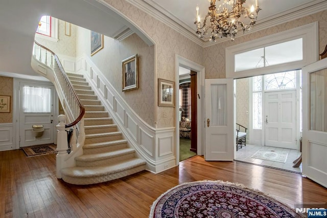 entryway with a decorative wall, wood-type flooring, an inviting chandelier, and wallpapered walls