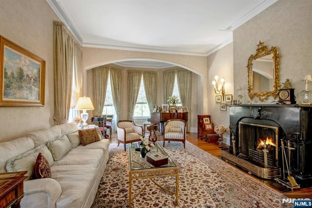 living room featuring arched walkways, a premium fireplace, crown molding, and wood finished floors