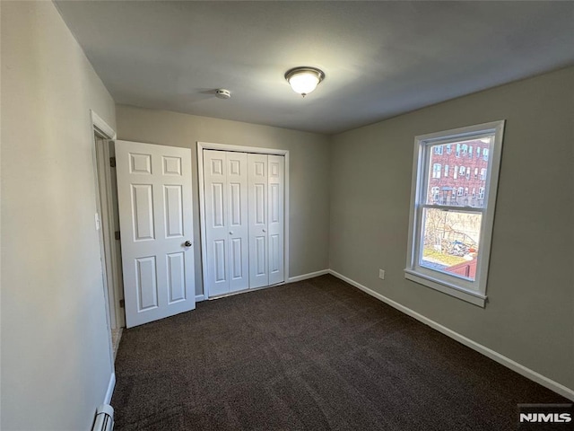 unfurnished bedroom with baseboard heating, a closet, and dark carpet