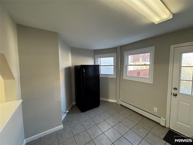 interior space with baseboard heating, black refrigerator, light tile patterned flooring, and plenty of natural light