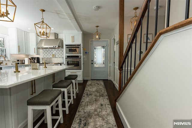 kitchen with a kitchen bar, pendant lighting, white cabinets, dark hardwood / wood-style floors, and range hood