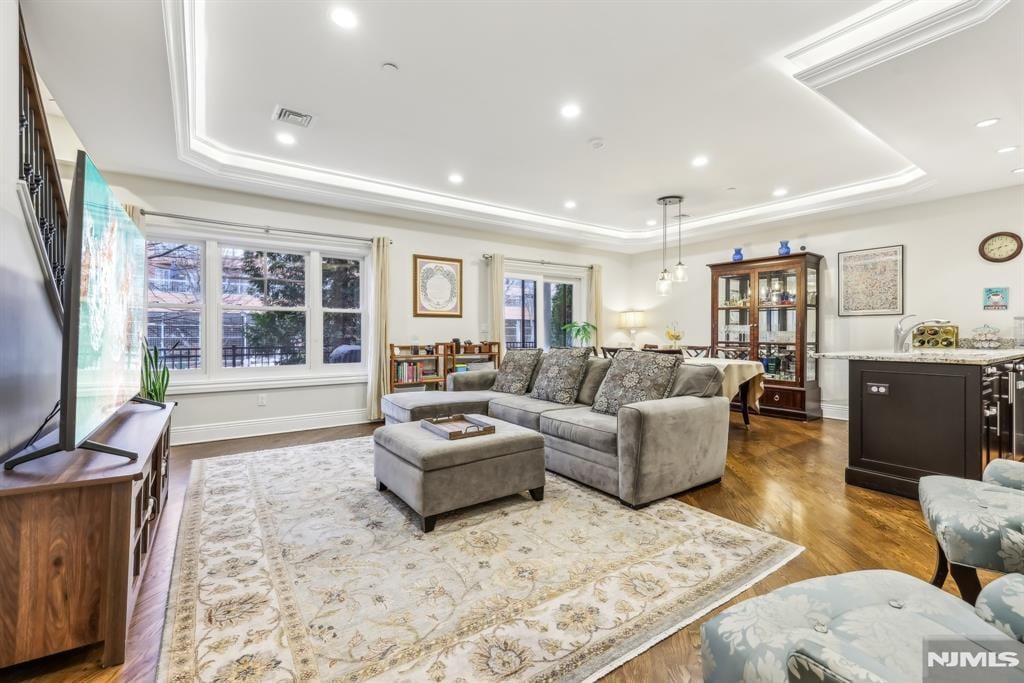 living room with a raised ceiling, crown molding, and dark wood-type flooring