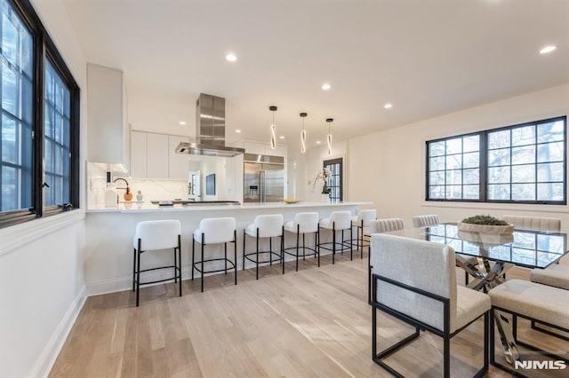 kitchen with island exhaust hood, kitchen peninsula, stainless steel built in refrigerator, white cabinets, and hanging light fixtures