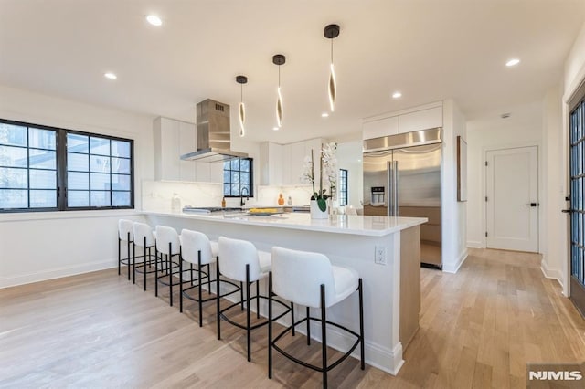 kitchen with built in fridge, kitchen peninsula, pendant lighting, extractor fan, and white cabinets