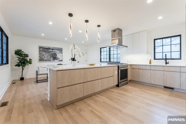 kitchen featuring pendant lighting, light brown cabinets, ventilation hood, stainless steel stove, and light hardwood / wood-style flooring