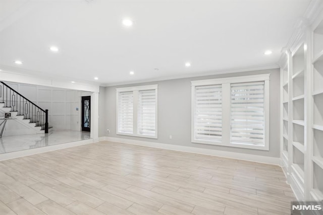 unfurnished living room featuring built in shelves, crown molding, and light wood-type flooring