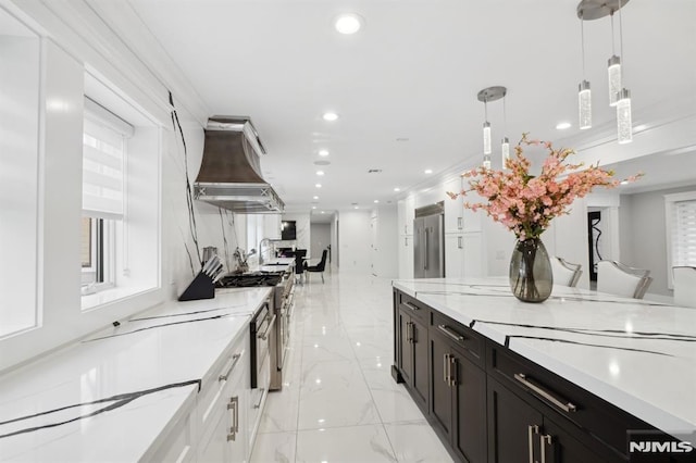 kitchen featuring stainless steel built in fridge, hanging light fixtures, wall chimney exhaust hood, light stone counters, and white cabinetry