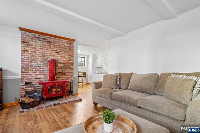 living room featuring sink, beam ceiling, light hardwood / wood-style floors, and a wood stove