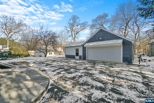 view of snow covered exterior featuring a garage and an outbuilding