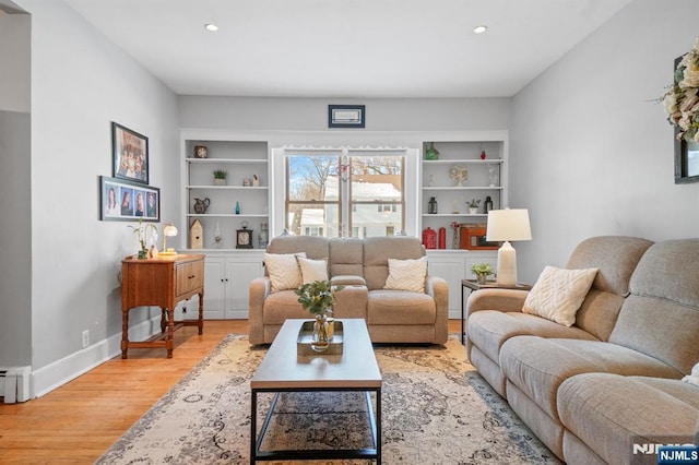 living room featuring built in shelves, baseboard heating, and light hardwood / wood-style floors