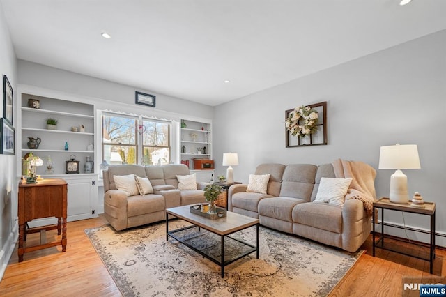 living room with built in shelves, a baseboard heating unit, and light wood-type flooring