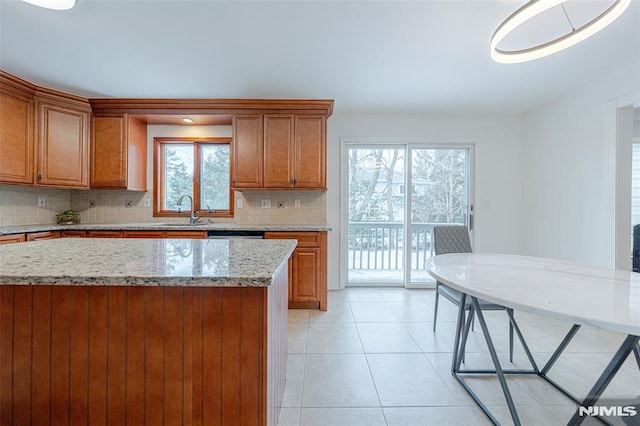 kitchen featuring tasteful backsplash, a kitchen island, sink, light stone countertops, and light tile patterned floors