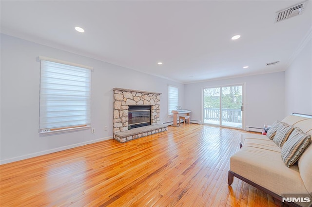 living room featuring a stone fireplace, ornamental molding, and light hardwood / wood-style flooring