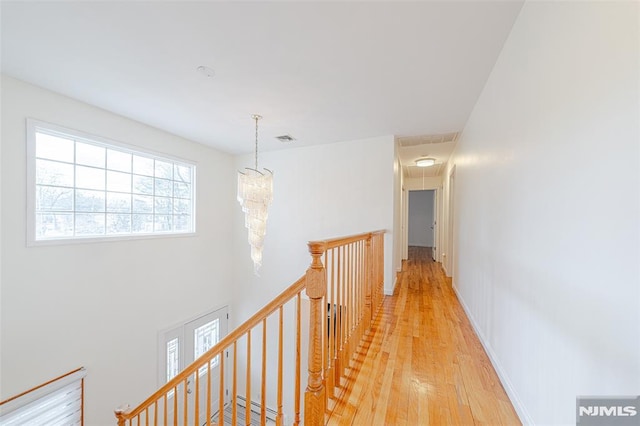 corridor with light hardwood / wood-style floors and a notable chandelier