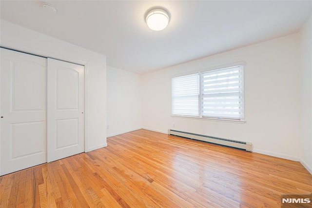 unfurnished bedroom featuring a baseboard heating unit, a closet, and light hardwood / wood-style floors