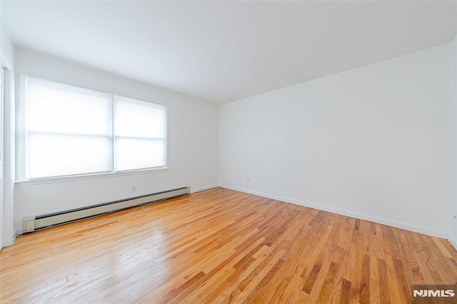 spare room featuring baseboard heating and light hardwood / wood-style flooring