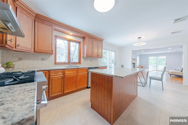 kitchen with light stone countertops, a center island, sink, stainless steel dishwasher, and range hood