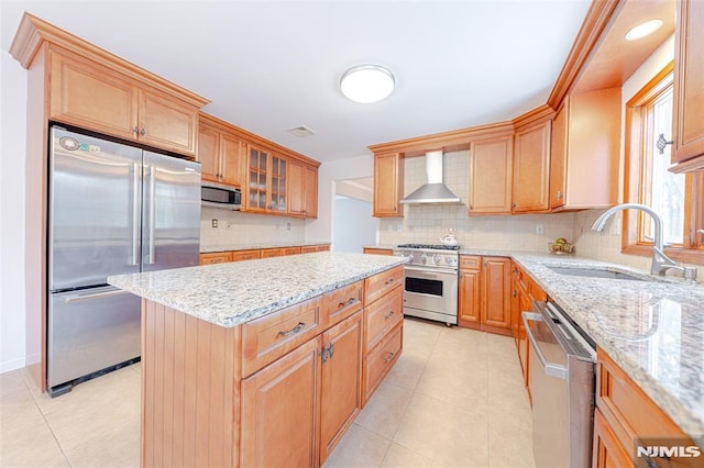 kitchen with wall chimney range hood, tasteful backsplash, light stone countertops, high quality appliances, and sink