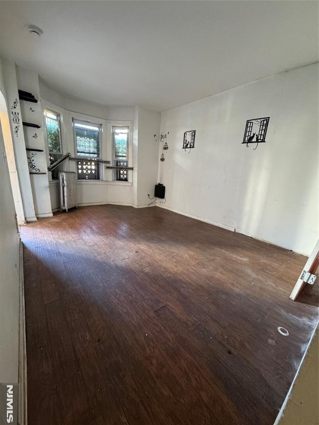 unfurnished living room with a wealth of natural light, dark hardwood / wood-style flooring, and radiator