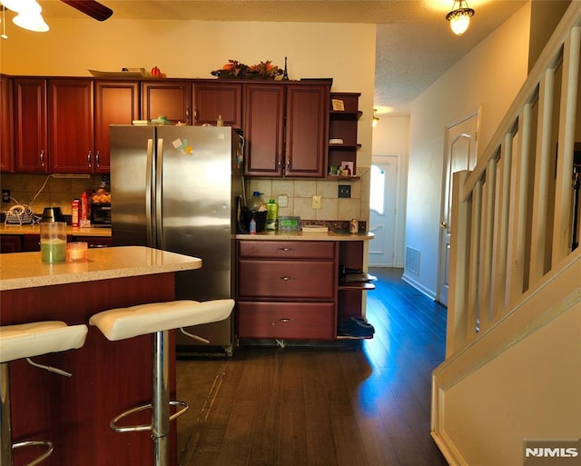 kitchen with dark hardwood / wood-style floors, stainless steel fridge, a kitchen bar, and tasteful backsplash