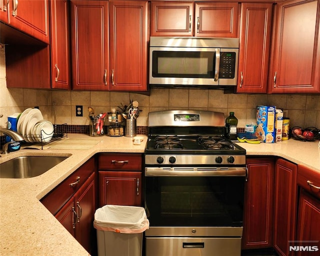 kitchen with decorative backsplash, appliances with stainless steel finishes, light stone counters, and sink