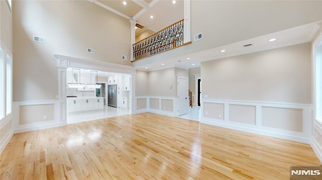 unfurnished living room with a high ceiling, light hardwood / wood-style flooring, and ornamental molding