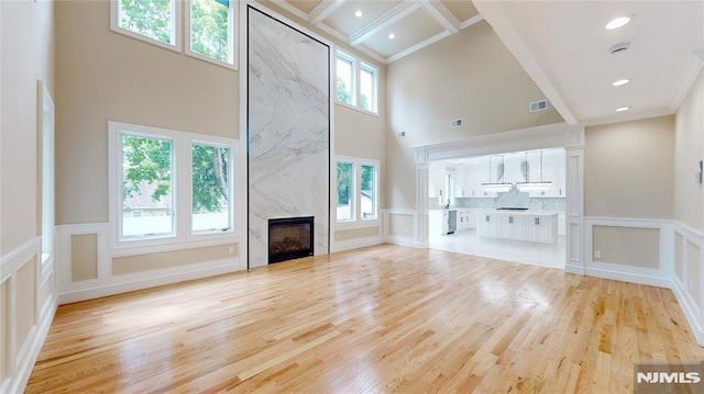 unfurnished living room featuring coffered ceiling, light hardwood / wood-style flooring, a premium fireplace, beamed ceiling, and a high ceiling