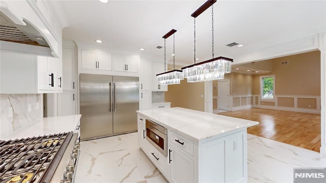 kitchen with pendant lighting, built in appliances, white cabinetry, and custom exhaust hood