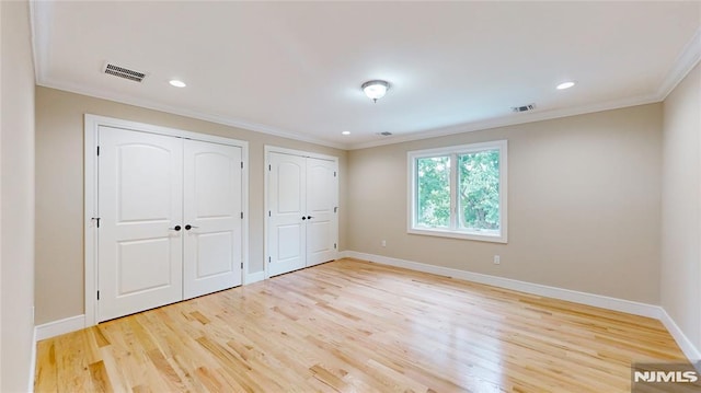 unfurnished bedroom with two closets, crown molding, and light hardwood / wood-style flooring