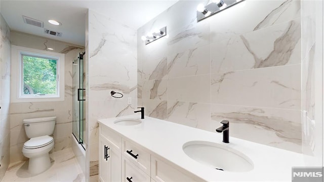 bathroom featuring vanity, toilet, a shower with door, and tile walls