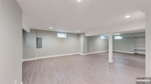 basement featuring electric panel, a healthy amount of sunlight, and light hardwood / wood-style floors