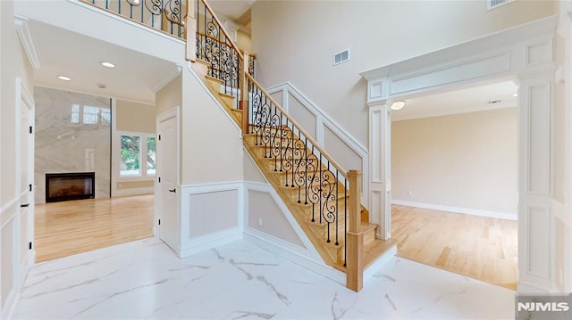 stairs with ornate columns, crown molding, and a fireplace