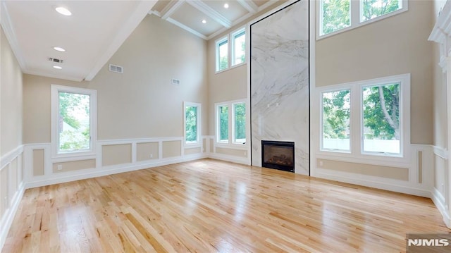 unfurnished living room with a fireplace, a healthy amount of sunlight, crown molding, and a high ceiling