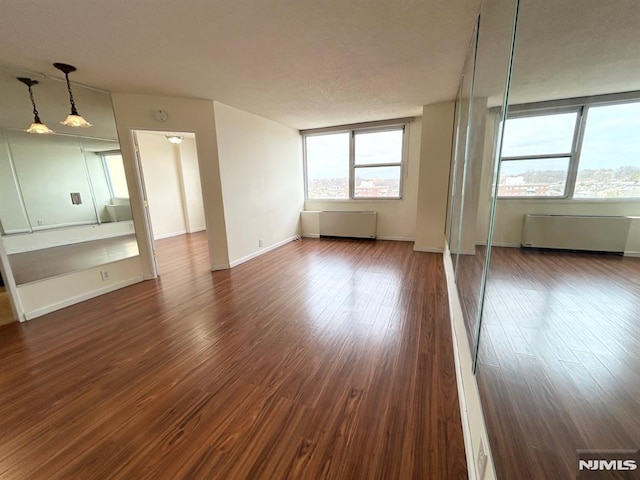 unfurnished room with radiator, a wealth of natural light, and dark wood-type flooring