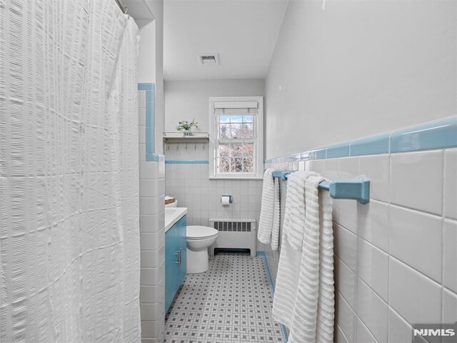 bathroom featuring tile walls, toilet, radiator heating unit, and vanity