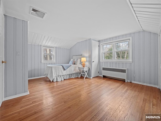 unfurnished bedroom with lofted ceiling, radiator heating unit, and light hardwood / wood-style floors