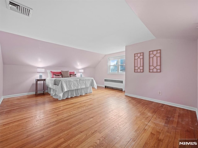 unfurnished bedroom with radiator, light wood-type flooring, and vaulted ceiling