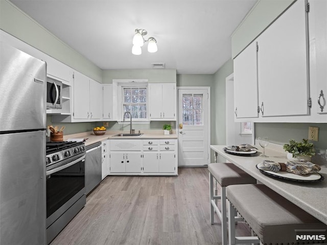 kitchen featuring appliances with stainless steel finishes, white cabinetry, light hardwood / wood-style floors, and sink